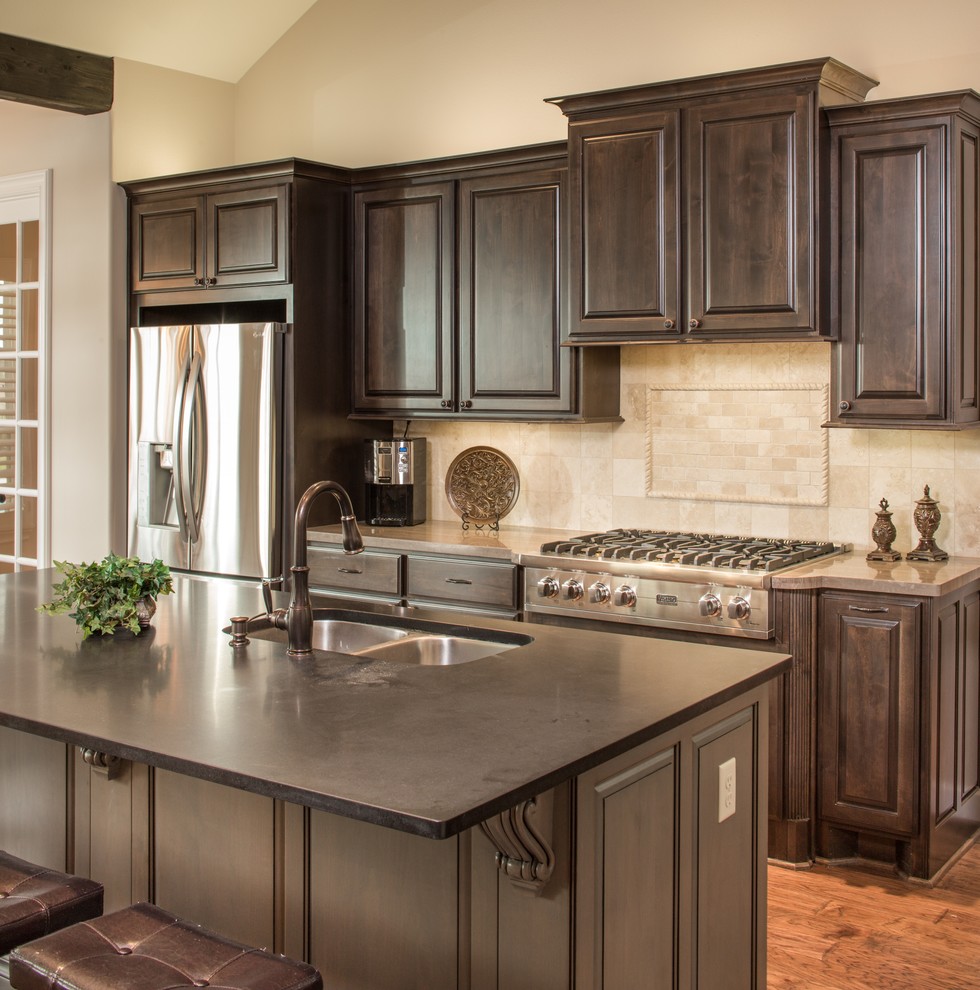 Offene, Mittelgroße Klassische Küche in L-Form mit Unterbauwaschbecken, profilierten Schrankfronten, Granit-Arbeitsplatte, Küchenrückwand in Beige, Küchengeräten aus Edelstahl, braunem Holzboden und Kücheninsel in Houston