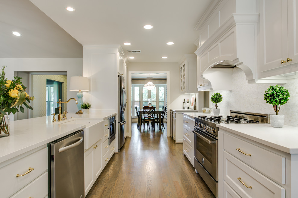 Inspiration for a classic galley kitchen in Dallas with a belfast sink, shaker cabinets, white cabinets, white splashback, stainless steel appliances, light hardwood flooring and a breakfast bar.