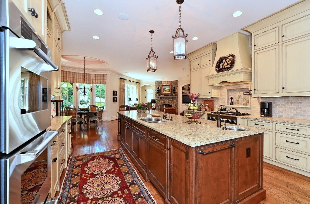 Exempel på ett stort klassiskt kök, med en undermonterad diskho, luckor med profilerade fronter, beige skåp, granitbänkskiva, rosa stänkskydd, stänkskydd i tegel, rostfria vitvaror, mellanmörkt trägolv och en köksö
