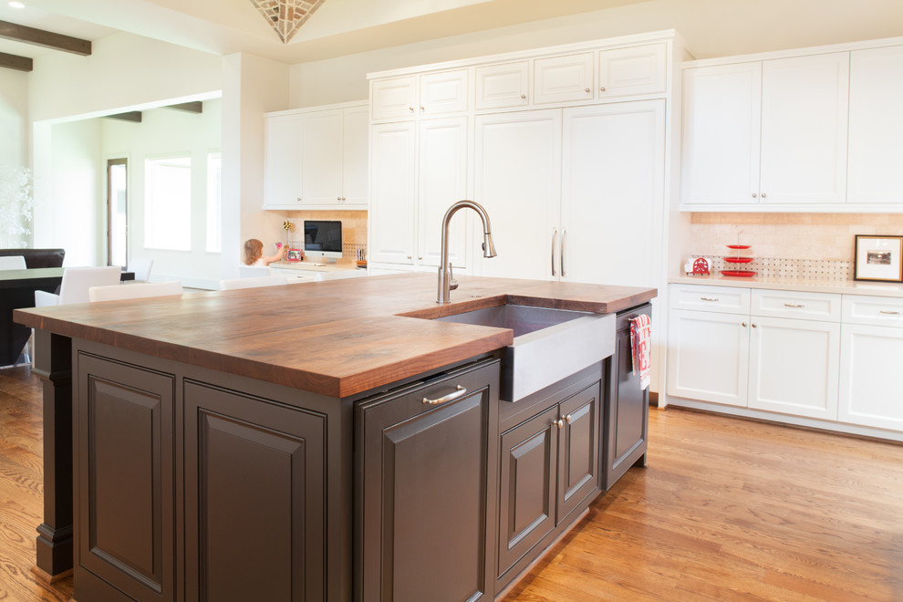 Large elegant u-shaped dark wood floor and brown floor eat-in kitchen photo in Houston with a farmhouse sink, raised-panel cabinets, brown cabinets, wood countertops, beige backsplash, stone tile backsplash, paneled appliances and an island