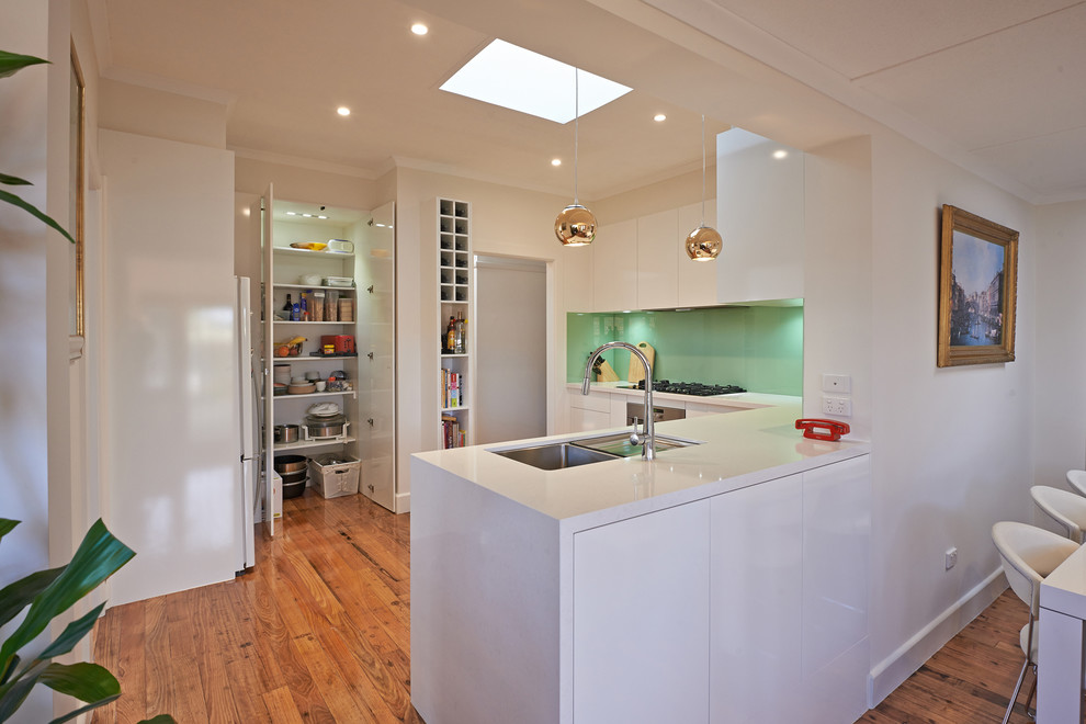 Inspiration for a mid-sized contemporary u-shaped dark wood floor enclosed kitchen remodel in Melbourne with a drop-in sink, flat-panel cabinets, white cabinets, quartz countertops, green backsplash, glass sheet backsplash, stainless steel appliances and an island