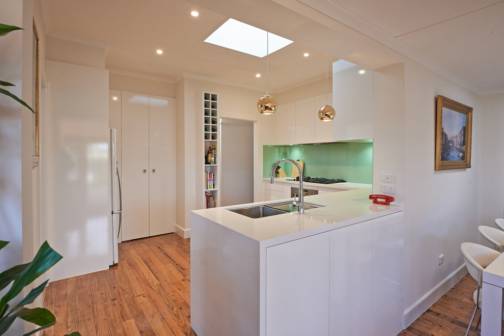 Enclosed kitchen - mid-sized contemporary u-shaped dark wood floor enclosed kitchen idea in Melbourne with a drop-in sink, flat-panel cabinets, white cabinets, quartz countertops, green backsplash, glass sheet backsplash, stainless steel appliances and an island