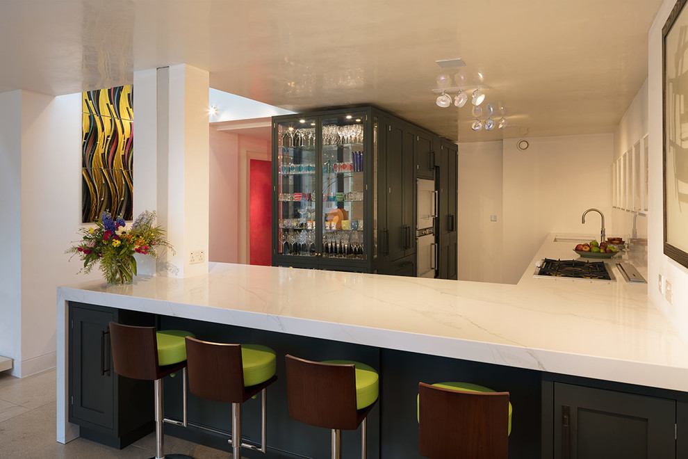 Large contemporary l-shaped home bar in London with a submerged sink, glass-front cabinets, marble worktops, white worktops and green cabinets.