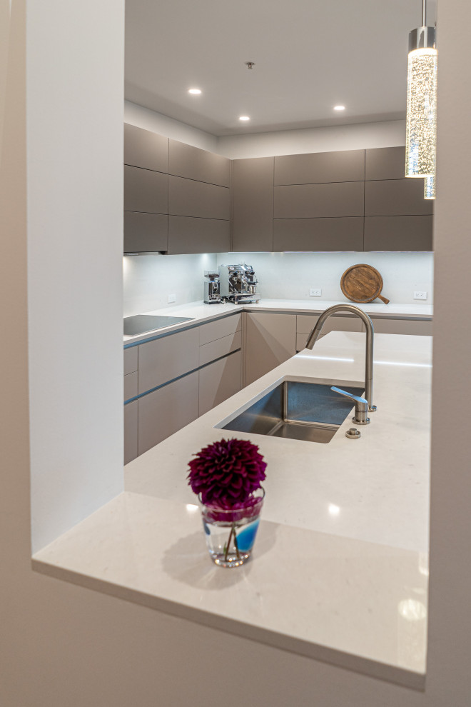 Inspiration for a mid-sized modern l-shaped medium tone wood floor and brown floor open concept kitchen remodel in Portland with an undermount sink, flat-panel cabinets, beige cabinets, quartz countertops, white backsplash, quartz backsplash, paneled appliances, a peninsula and white countertops