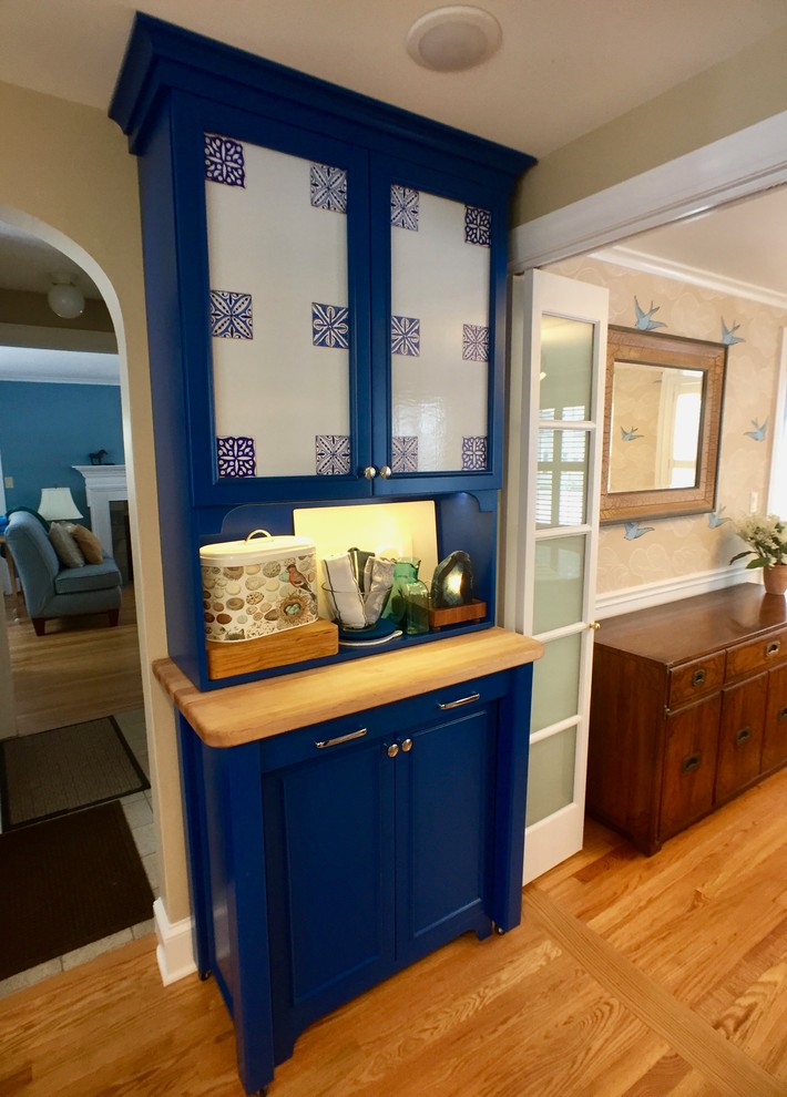 Cette photo montre une cuisine éclectique en U avec un placard avec porte à panneau encastré, des portes de placard bleues, un plan de travail en bois, une crédence bleue et parquet clair.