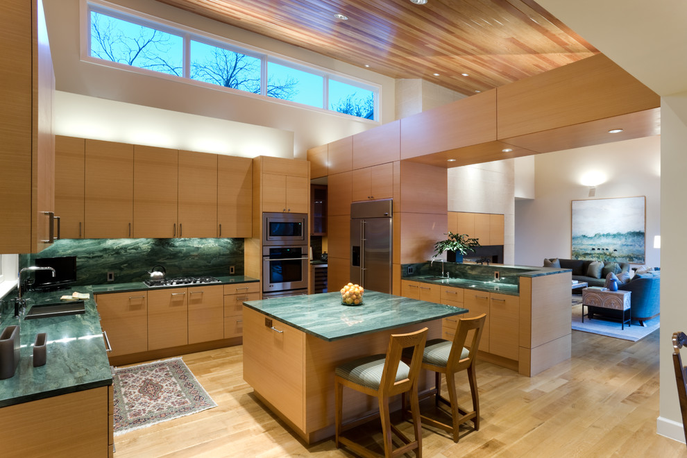 Bild på ett funkis u-kök, med en integrerad diskho, släta luckor, skåp i ljust trä, bänkskiva i täljsten, grönt stänkskydd, stänkskydd i sten och rostfria vitvaror