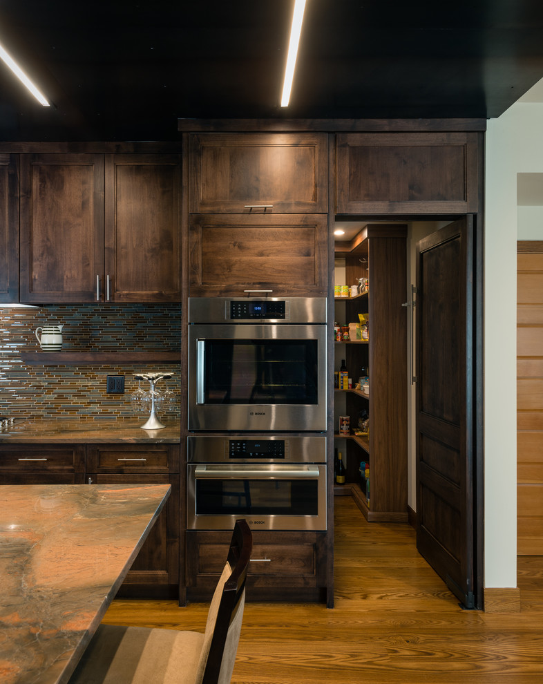 Inspiration for a mid-sized modern galley medium tone wood floor and brown floor open concept kitchen remodel in Baltimore with dark wood cabinets, an undermount sink, flat-panel cabinets, granite countertops, brown backsplash, glass tile backsplash, paneled appliances and an island