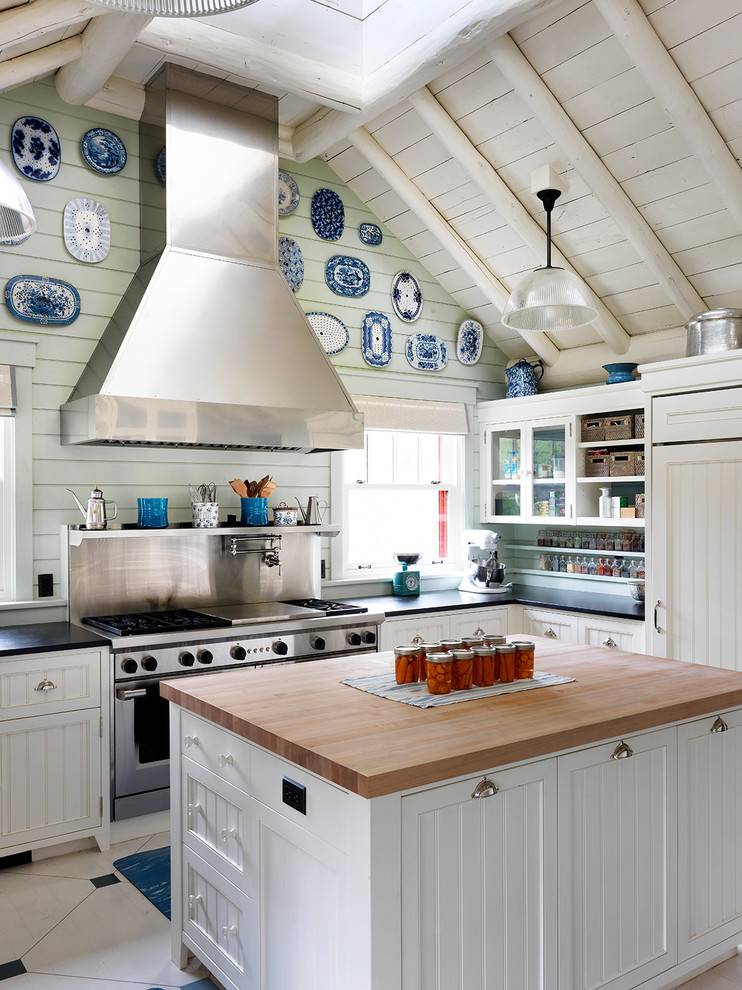 他の地域にあるラスティックスタイルのおしゃれなキッチン (落し込みパネル扉のキャビネット、白いキャビネット、木材カウンター、シルバーの調理設備、マルチカラーの床) の写真