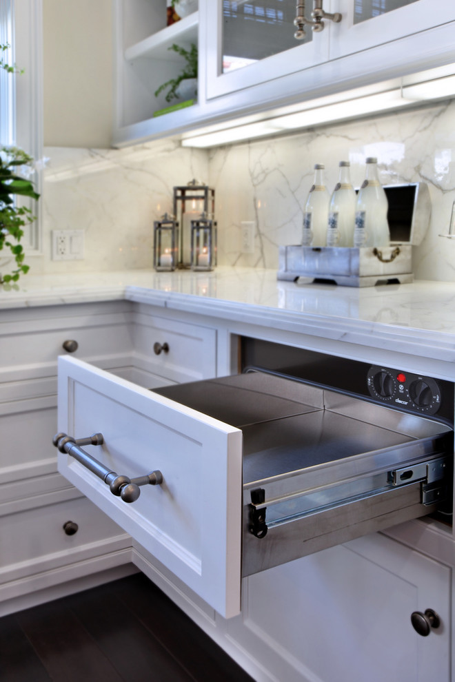 Foto på ett maritimt kök, med vita skåp, marmorbänkskiva, stänkskydd i sten, integrerade vitvaror, mörkt trägolv och en köksö