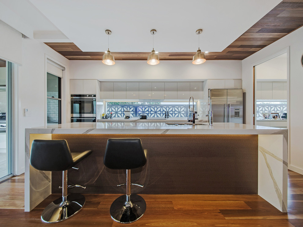 Mittelgroße, Zweizeilige Moderne Küche mit Doppelwaschbecken, weißen Schränken, Rückwand-Fenster, braunem Holzboden, Kücheninsel, braunem Boden, flächenbündigen Schrankfronten, Küchengeräten aus Edelstahl und bunter Arbeitsplatte in Brisbane