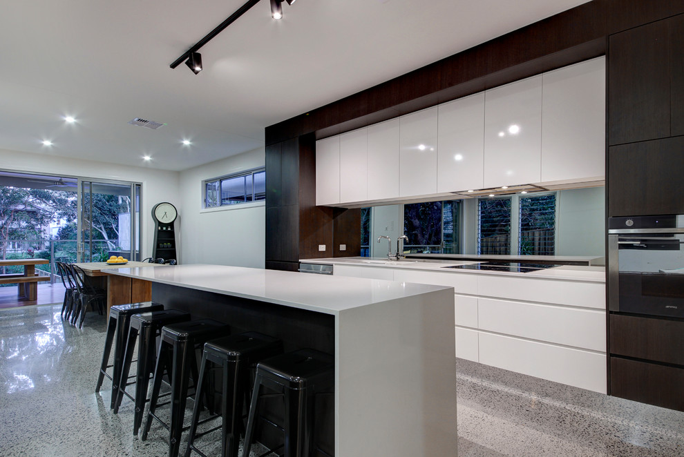 Exempel på ett mellanstort modernt kök, med en undermonterad diskho, släta luckor, vita skåp, laminatbänkskiva, stänkskydd med metallisk yta, glaspanel som stänkskydd, rostfria vitvaror, betonggolv och en köksö