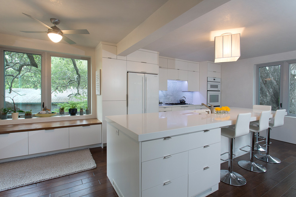Ejemplo de cocina comedor actual con armarios con paneles lisos, puertas de armario blancas, salpicadero blanco, salpicadero de losas de piedra y electrodomésticos blancos