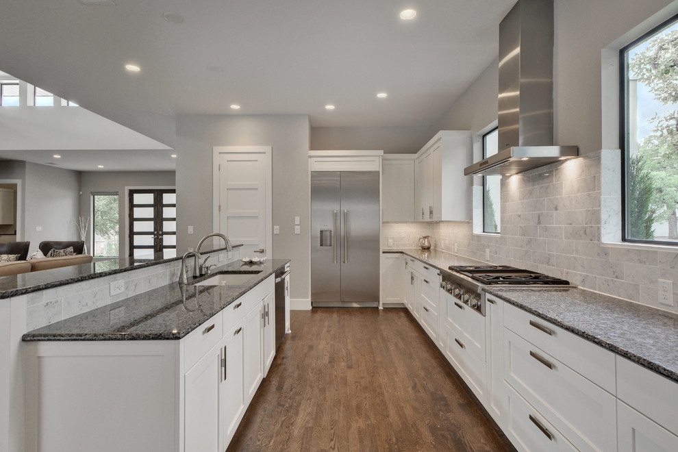Photo of a large modern galley open plan kitchen in Austin with a submerged sink, shaker cabinets, white cabinets, granite worktops, multi-coloured splashback, metro tiled splashback, stainless steel appliances, medium hardwood flooring and an island.
