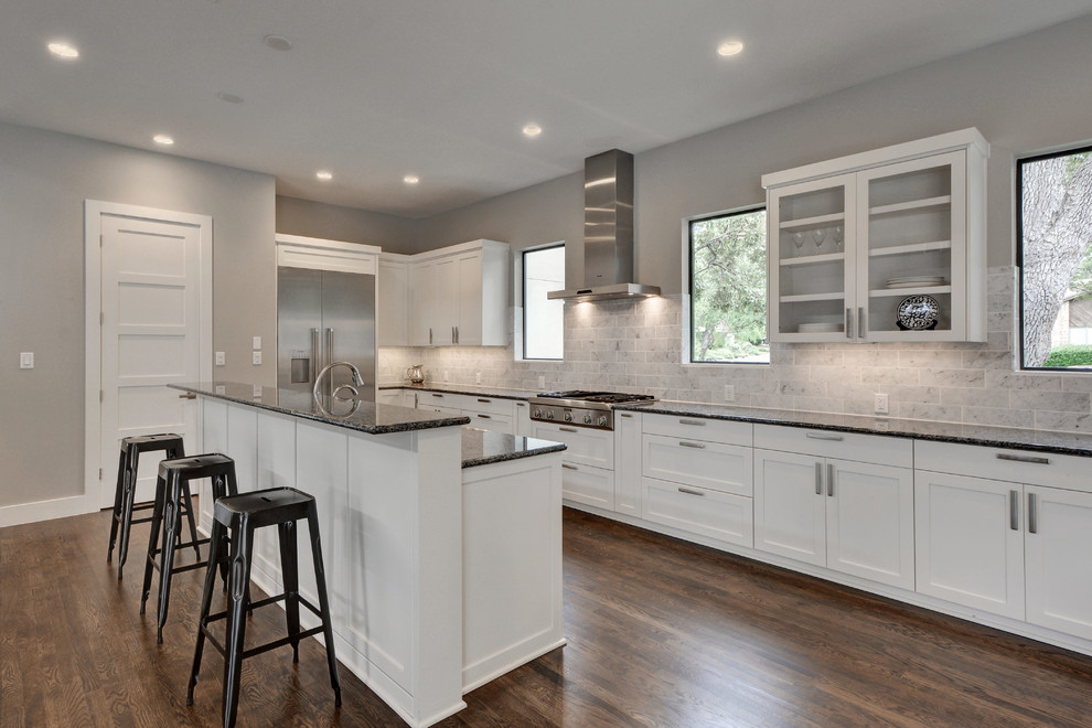 Open concept kitchen - large modern galley medium tone wood floor open concept kitchen idea in Austin with an undermount sink, shaker cabinets, white cabinets, granite countertops, multicolored backsplash, subway tile backsplash, stainless steel appliances and an island
