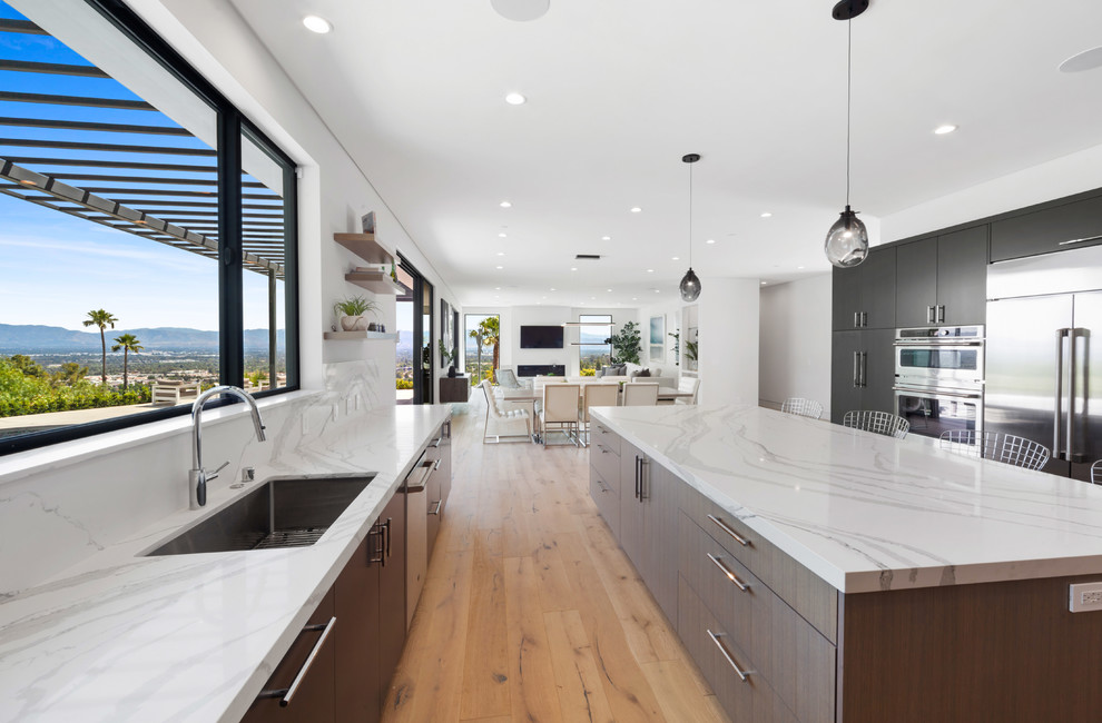 Inspiration for a large contemporary u-shaped kitchen/diner in Los Angeles with a submerged sink, stainless steel appliances, an island, engineered stone countertops, white splashback, stone slab splashback, light hardwood flooring and white worktops.