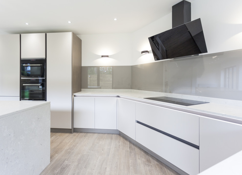 Bild på ett mellanstort funkis grå grått kök, med en undermonterad diskho, släta luckor, grå skåp, bänkskiva i kvartsit, brunt stänkskydd, glaspanel som stänkskydd, svarta vitvaror, mellanmörkt trägolv, en köksö och brunt golv