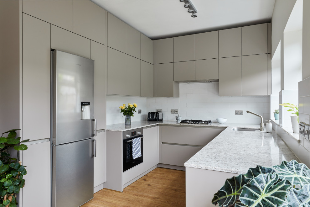 Design ideas for a medium sized contemporary u-shaped kitchen/diner in London with a submerged sink, flat-panel cabinets, grey cabinets, quartz worktops, white splashback, ceramic splashback, stainless steel appliances, vinyl flooring, no island, brown floors and multicoloured worktops.