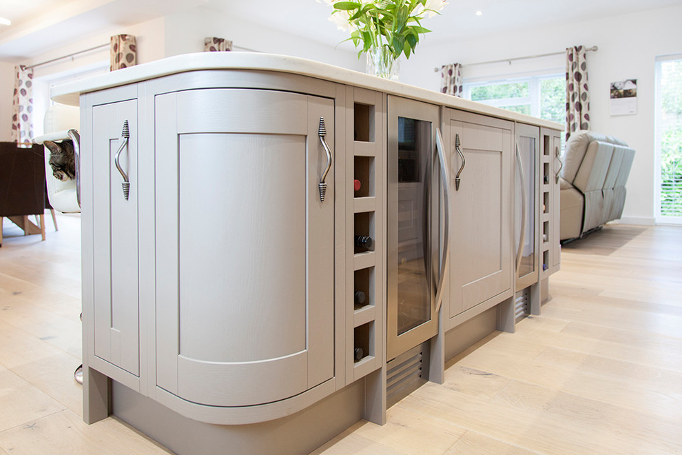 Large classic u-shaped open plan kitchen in Wiltshire with grey cabinets, quartz worktops, stone slab splashback, black appliances, light hardwood flooring, an island and brown floors.