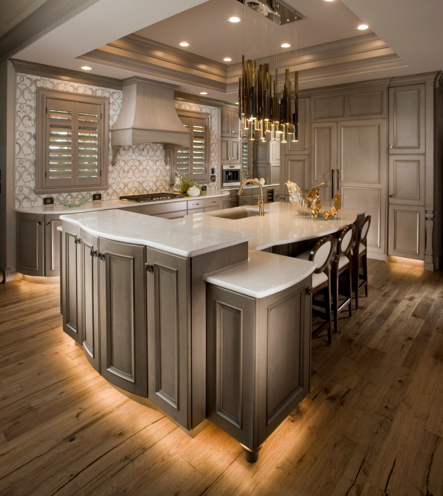 Large traditional open plan kitchen in Wichita with a single-bowl sink, recessed-panel cabinets, beige cabinets, engineered stone countertops, beige splashback, porcelain splashback, integrated appliances, medium hardwood flooring, an island, brown floors and white worktops.