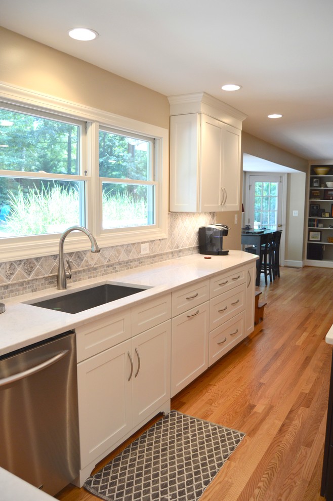 Photo of a large traditional l-shaped kitchen/diner in DC Metro with a submerged sink, shaker cabinets, white cabinets, engineered stone countertops, grey splashback, ceramic splashback, stainless steel appliances, light hardwood flooring and an island.