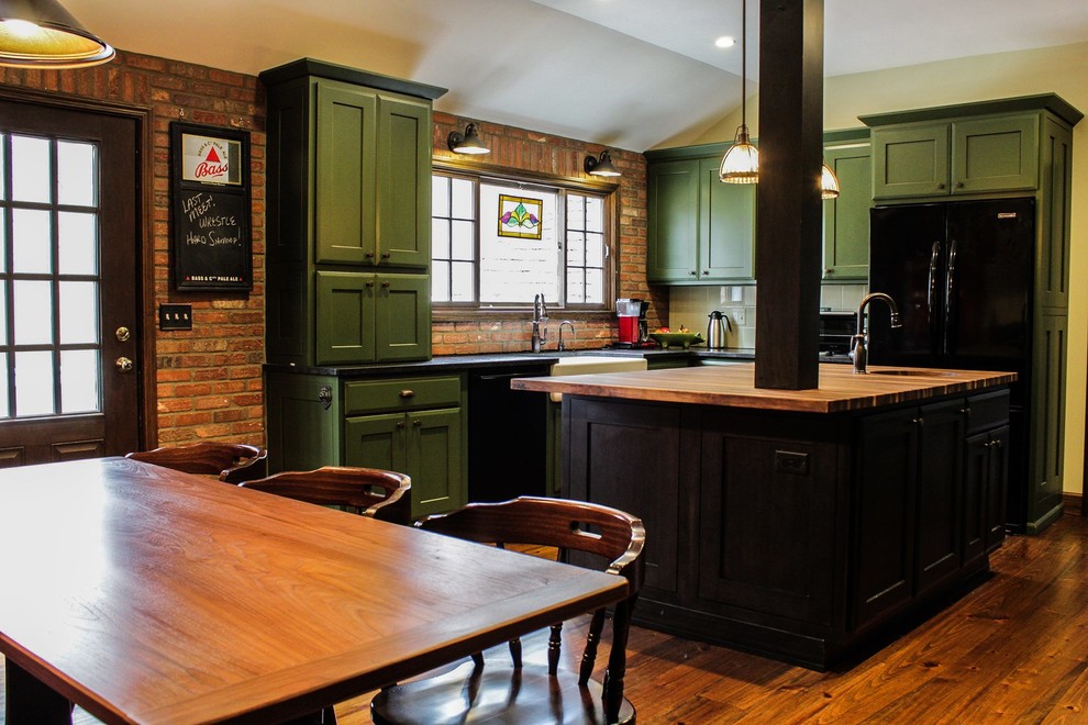 Eklektisk inredning av ett kök, med en rustik diskho, skåp i shakerstil, gröna skåp, granitbänkskiva, grönt stänkskydd, svarta vitvaror, mellanmörkt trägolv, en köksö och brunt golv