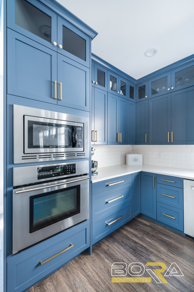 Large l-shaped kitchen/diner in Seattle with a submerged sink, shaker cabinets, blue cabinets, engineered stone countertops, white splashback, ceramic splashback, stainless steel appliances, marble flooring, an island, brown floors and white worktops.