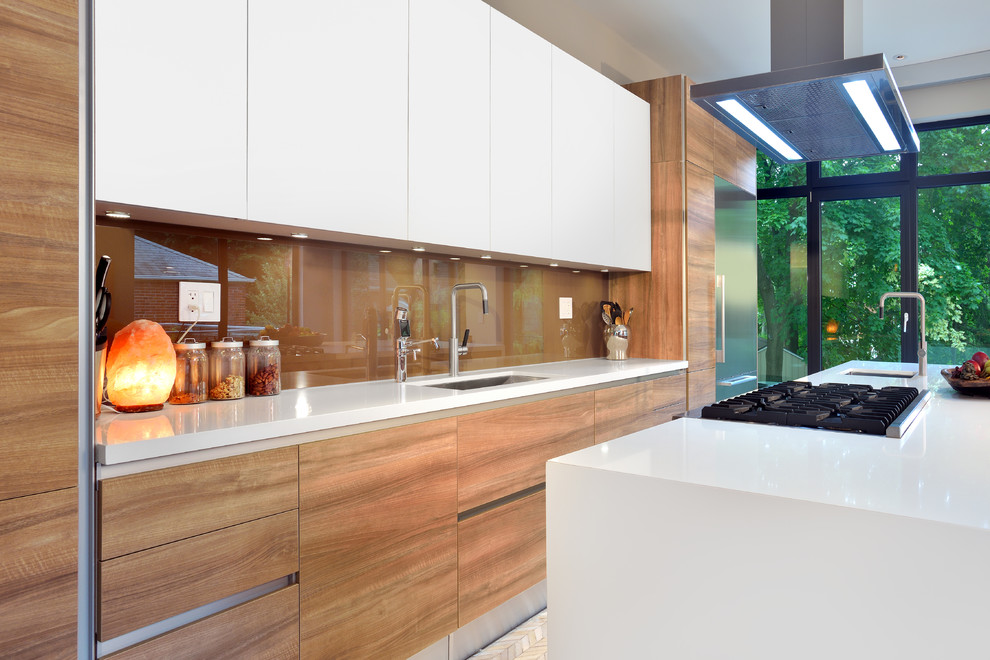 Bild på ett funkis kök, med en enkel diskho, släta luckor, skåp i mellenmörkt trä, bänkskiva i kvartsit, brunt stänkskydd, stänkskydd i sten, rostfria vitvaror och en köksö