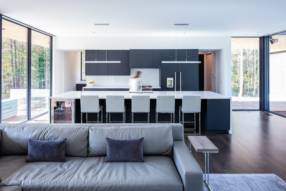 Inspiration for a modern galley open plan kitchen in Charlotte with a submerged sink, black cabinets, integrated appliances, dark hardwood flooring, an island, brown floors and white worktops.