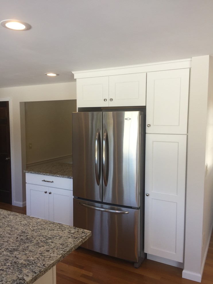 Ejemplo de cocina clásica, de tamaño medio, con fregadero bajoencimera, armarios estilo shaker, puertas de armario blancas, encimera de granito, salpicadero beige, salpicadero de azulejos de porcelana, electrodomésticos de acero inoxidable, suelo de madera clara y una isla