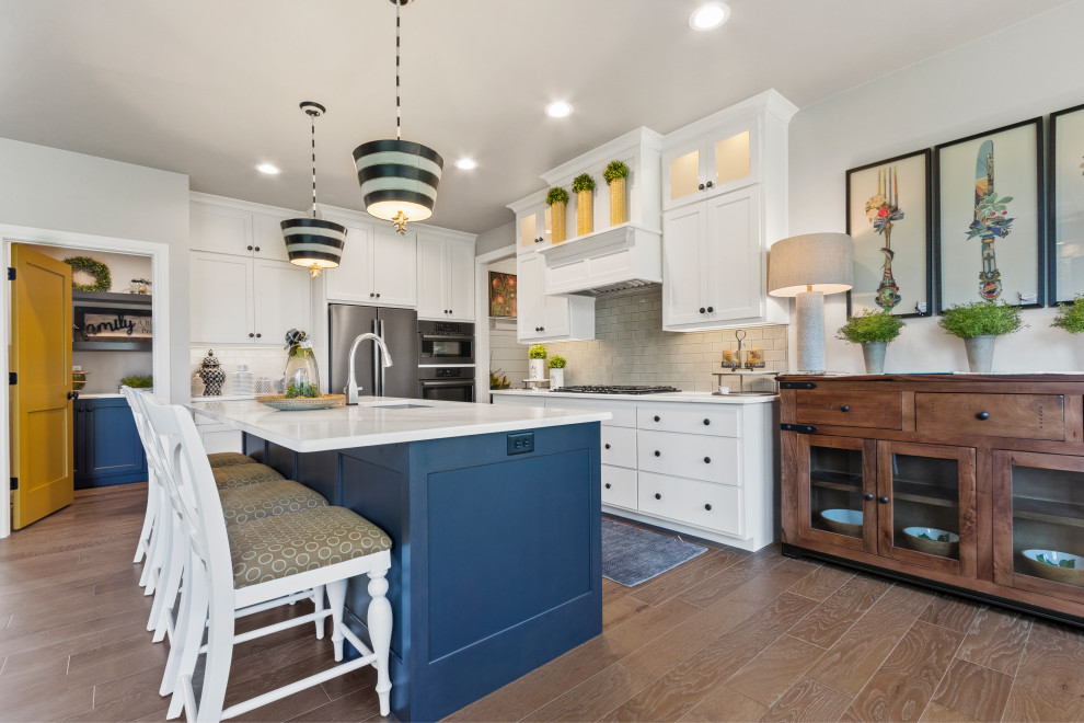 Bild på ett mellanstort maritimt vit vitt kök, med en undermonterad diskho, skåp i shakerstil, vita skåp, bänkskiva i kvarts, grått stänkskydd, stänkskydd i keramik, rostfria vitvaror, mellanmörkt trägolv, en köksö och brunt golv
