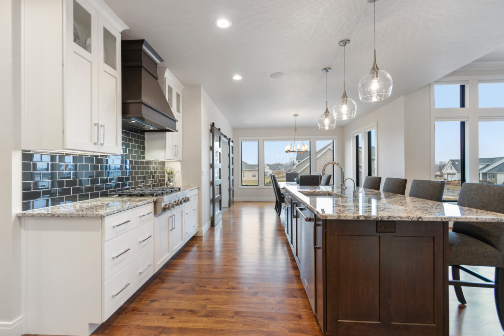 Example of a mid-sized transitional l-shaped medium tone wood floor and brown floor eat-in kitchen design in Other with an undermount sink, shaker cabinets, white cabinets, granite countertops, blue backsplash, subway tile backsplash, stainless steel appliances, multicolored countertops and an island