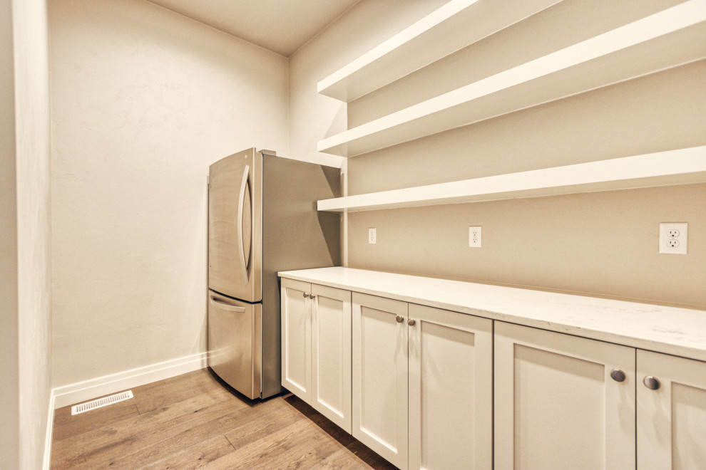 Klassisk inredning av ett stort vit vitt kök, med en undermonterad diskho, skåp i shakerstil, vita skåp, bänkskiva i kvarts, vitt stänkskydd, stänkskydd i keramik, rostfria vitvaror, mellanmörkt trägolv, en köksö och brunt golv