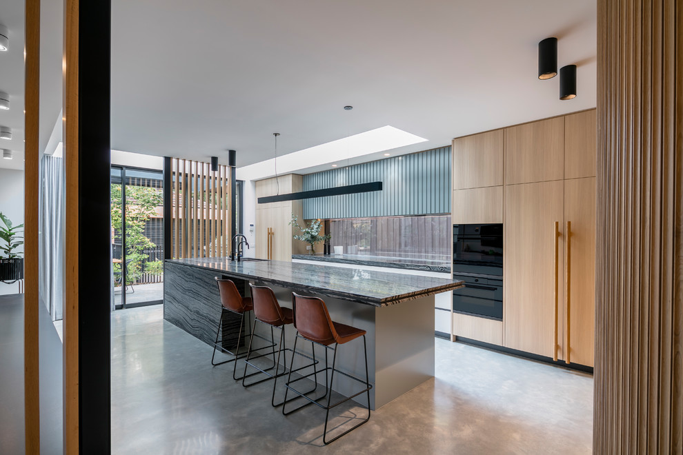 Inspiration for a large contemporary galley open plan kitchen in Melbourne with a built-in sink, light wood cabinets, window splashback, black appliances, concrete flooring, an island, grey floors, flat-panel cabinets and grey worktops.
