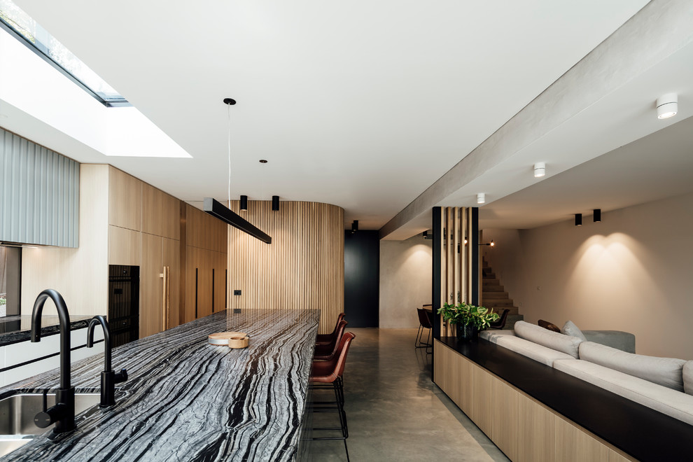 Réalisation d'une grande cuisine ouverte parallèle minimaliste en bois clair avec un évier posé, fenêtre, un électroménager noir, sol en béton ciré, îlot, un sol gris et un plan de travail multicolore.