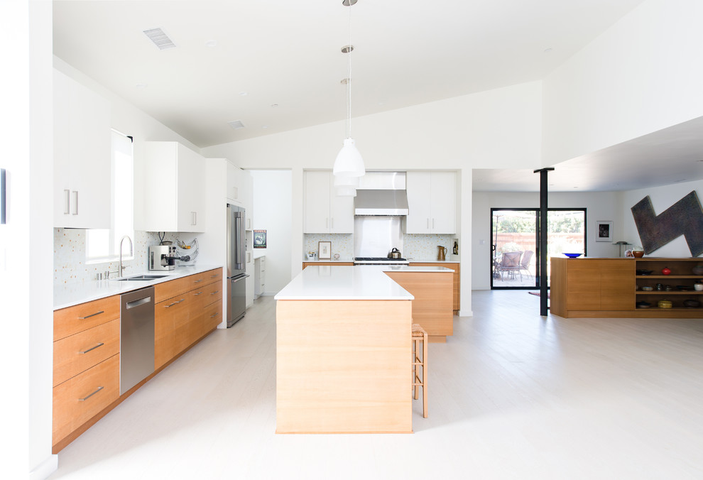 Photo of a large modern l-shaped open plan kitchen in Orange County with a submerged sink, flat-panel cabinets, white cabinets, engineered stone countertops, multi-coloured splashback, stainless steel appliances, light hardwood flooring, an island and mosaic tiled splashback.
