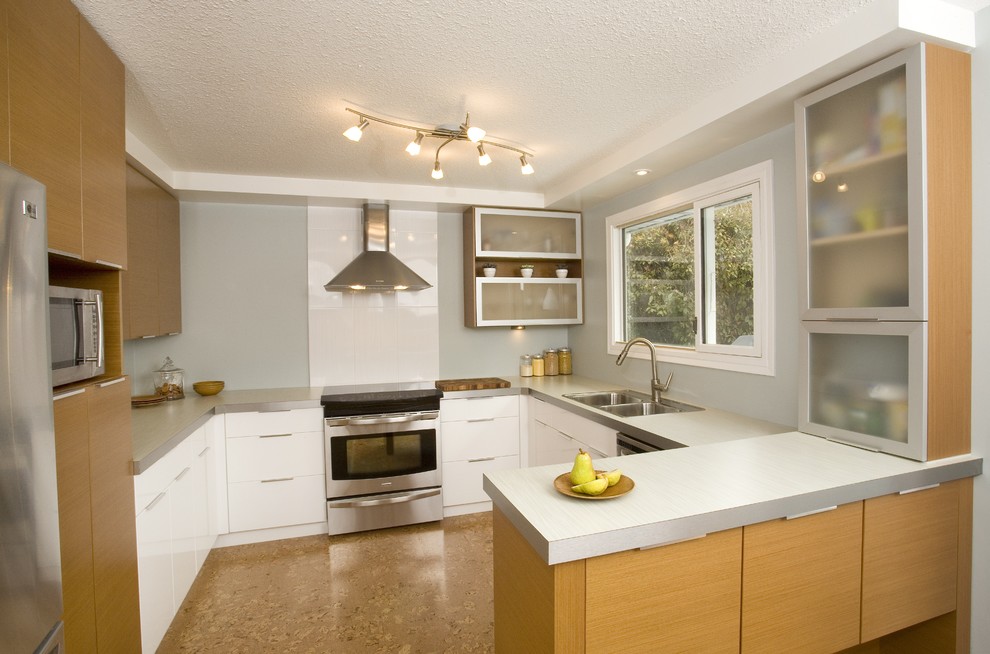 Bild på ett avskilt funkis grå grått l-kök, med en dubbel diskho, släta luckor, skåp i ljust trä, bänkskiva i betong, vitt stänkskydd, glaspanel som stänkskydd, rostfria vitvaror, korkgolv, en halv köksö och brunt golv