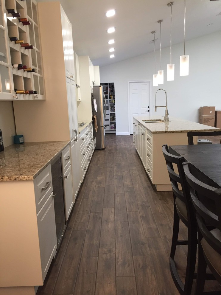 Mid-sized transitional single-wall medium tone wood floor and brown floor eat-in kitchen photo in Orlando with raised-panel cabinets, white cabinets, granite countertops, an island, beige countertops, an undermount sink and stainless steel appliances