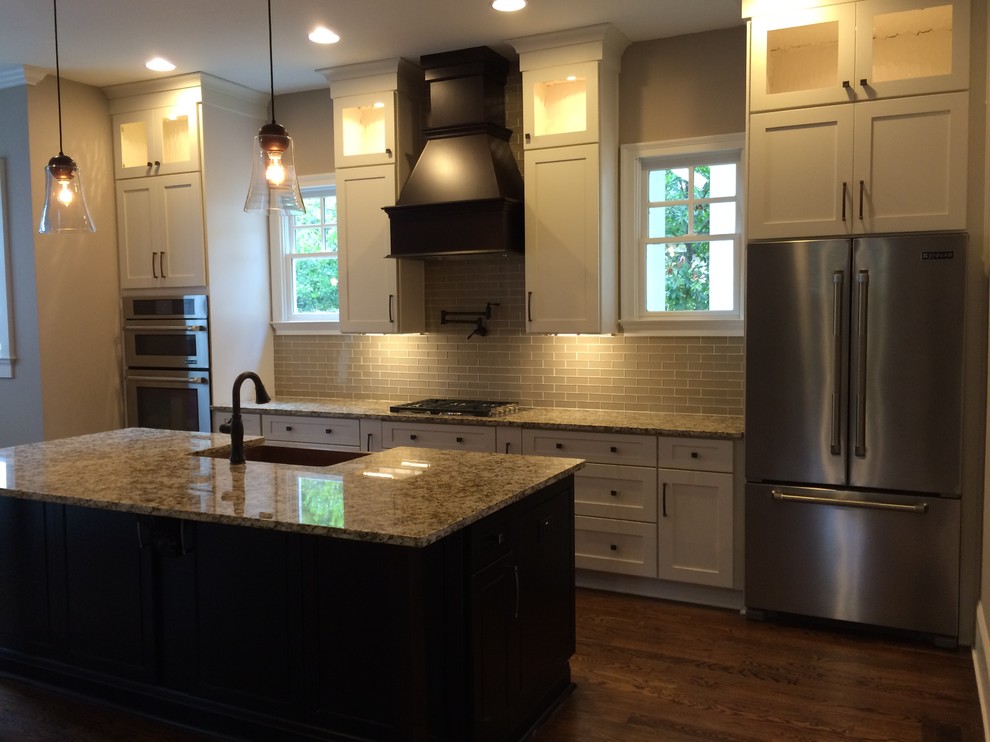 Mid-sized transitional single-wall dark wood floor kitchen photo in Atlanta with a farmhouse sink, shaker cabinets, white cabinets, granite countertops, beige backsplash, subway tile backsplash, stainless steel appliances and an island