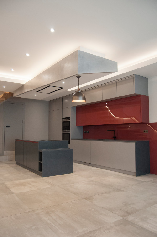 Foto på ett stort funkis grå linjärt kök med öppen planlösning, med en dubbel diskho, släta luckor, grå skåp, bänkskiva i kvartsit, rött stänkskydd, glaspanel som stänkskydd, svarta vitvaror, cementgolv, en köksö och grått golv