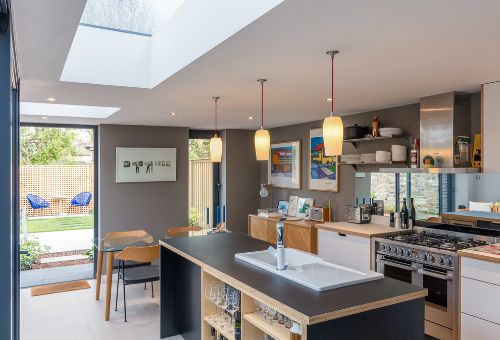 Inspiration for a medium sized modern single-wall kitchen/diner in London with a single-bowl sink, flat-panel cabinets, wood worktops, metallic splashback, mirror splashback, an island and grey floors.