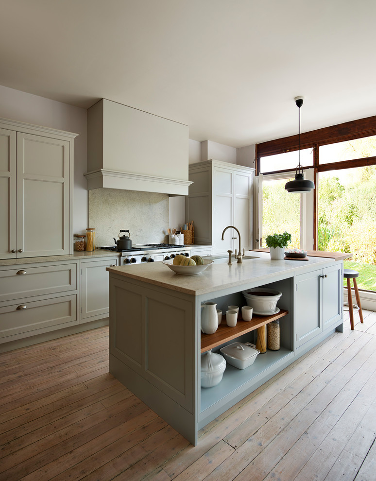 Cette photo montre une cuisine parallèle nature avec un placard avec porte à panneau surélevé, des portes de placard grises, une crédence grise, parquet clair, îlot et un sol marron.