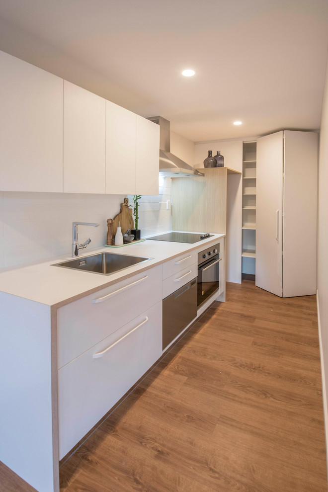 Design ideas for a small scandi single-wall enclosed kitchen in Christchurch with a single-bowl sink, flat-panel cabinets, white cabinets, laminate countertops, white splashback, metro tiled splashback, stainless steel appliances, vinyl flooring, no island, brown floors and white worktops.