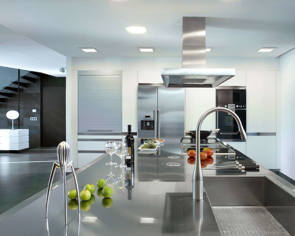 Diseño de cocina actual abierta con fregadero integrado, puertas de armario blancas, encimera de acero inoxidable y electrodomésticos de acero inoxidable