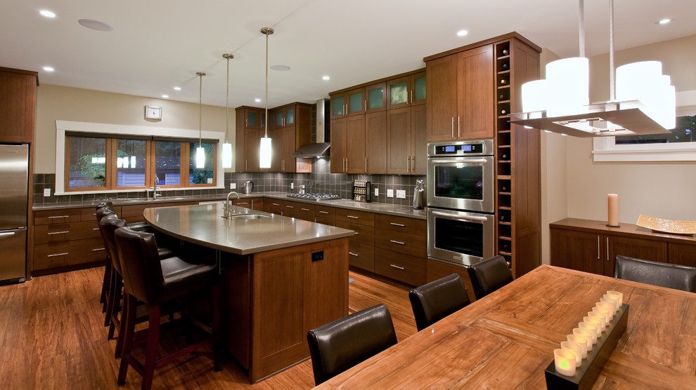Inspiration for a large contemporary l-shaped kitchen/diner in Vancouver with shaker cabinets, engineered stone countertops, a submerged sink, dark wood cabinets, stainless steel appliances, medium hardwood flooring, an island, brown floors, grey splashback and grey worktops.