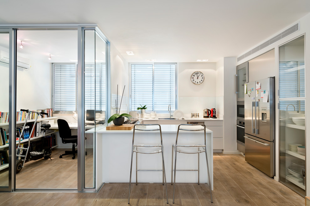 This is an example of a contemporary u-shaped kitchen in Tel Aviv with flat-panel cabinets, white cabinets, white splashback and stainless steel appliances.
