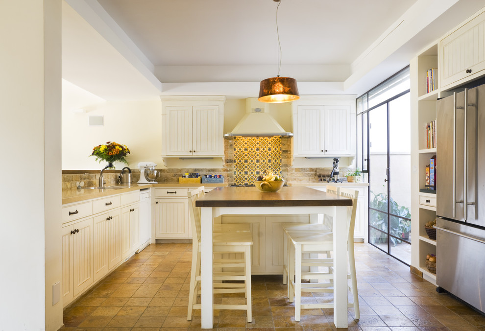 This is an example of a mediterranean l-shaped kitchen with stainless steel appliances, recessed-panel cabinets, white cabinets, multi-coloured splashback, mosaic tiled splashback and an island.
