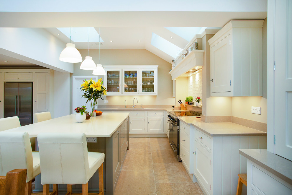 This is an example of a traditional l-shaped kitchen in London with a submerged sink, recessed-panel cabinets, white cabinets, white splashback, black appliances, an island, beige floors and beige worktops.