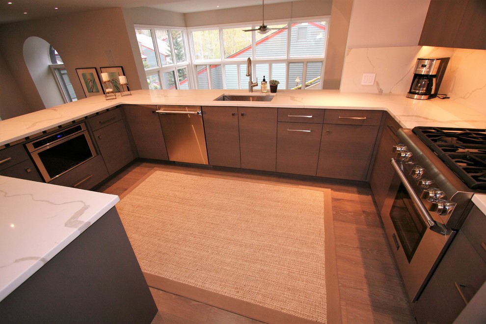 Foto på ett mellanstort funkis kök, med en undermonterad diskho, släta luckor, skåp i mellenmörkt trä, marmorbänkskiva, vitt stänkskydd, stänkskydd i marmor, rostfria vitvaror, mellanmörkt trägolv och en halv köksö