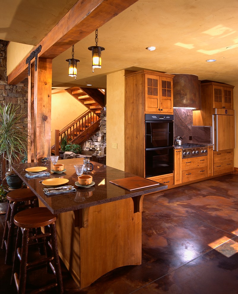 Rustik inredning av ett stort linjärt kök med öppen planlösning, med betonggolv, en köksö, släta luckor, skåp i ljust trä, granitbänkskiva och brunt golv