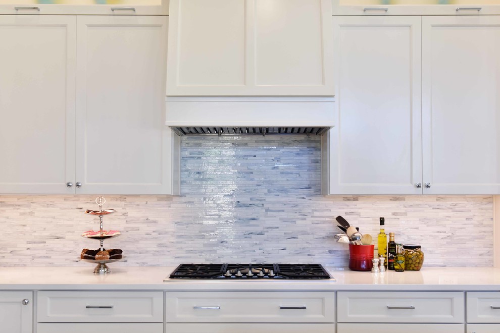Inredning av ett klassiskt stort grå grått kök, med en undermonterad diskho, luckor med infälld panel, vita skåp, bänkskiva i kvarts, vitt stänkskydd, stänkskydd i stenkakel, rostfria vitvaror, klinkergolv i porslin, en köksö och beiget golv